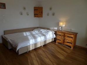 Une chambre avec un lit simple, un plancher en bois, une table de chevet avec une lampe et des éléments décoratifs sur les murs.
