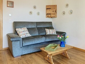 A grey sofa with patterned cushions, a wooden coffee table with a vase of tulips, and decorative plates on the wall. - Le Mont Blanc 8 by Interhome (Villars)