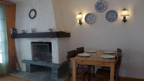 A dining area with a fireplace, wooden table, chairs, and wall-mounted decorative plates. - Le Mont Blanc 8 by Interhome (Villars)