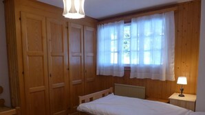 A bedroom with two single beds, wooden wardrobe, and a window with curtains. - Le Mont Blanc 8 by Interhome (Villars)