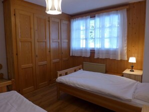 A bedroom with two single beds, wooden wardrobe, and a window with curtains.