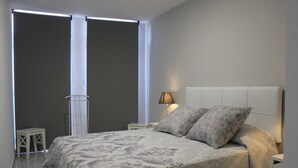 Un dormitorio con una cama grande, una mesita de noche, una lámpara y una ventana con cortinas.