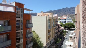 Un edificio residencial de varios pisos con balcones, vista despejada de la calle y montañas al fondo.
