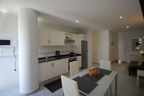 A modern kitchen with white cabinetry, a stainless steel refrigerator, and a dining area with a table and chairs.