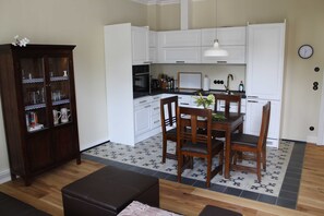 Een compacte keuken met witte kastjes, een eettafel met stoelen, en een donker houten kast met glazen deuren.