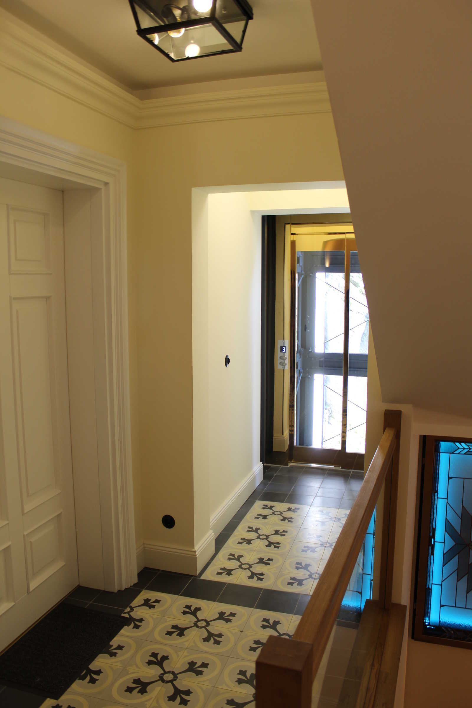 A hallway with patterned floor tiles, a white door, and a staircase with a wooden railing.