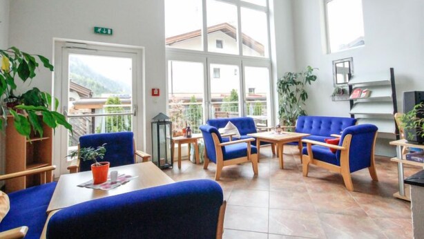 A bright room with large windows, blue upholstered chairs, a wooden table, and potted plants. - Falkner by Interhome (Längenfeld)