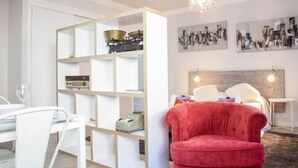 A modern living room with a red velvet armchair, a white bookshelf, and a dining area with a glass table and chairs. - Studio Mafra by Interhome (Mafra)