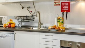A modern kitchen with white cabinets, a stainless steel sink, a microwave, a fruit basket, and a fire extinguisher. - Studio Mafra by Interhome (Mafra)