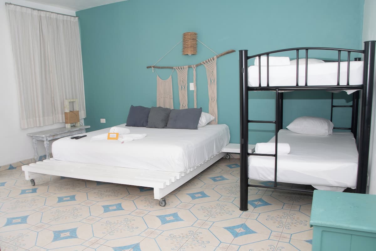A bedroom with a bed, a bunk bed, a nightstand, a lamp, and a window with curtains.