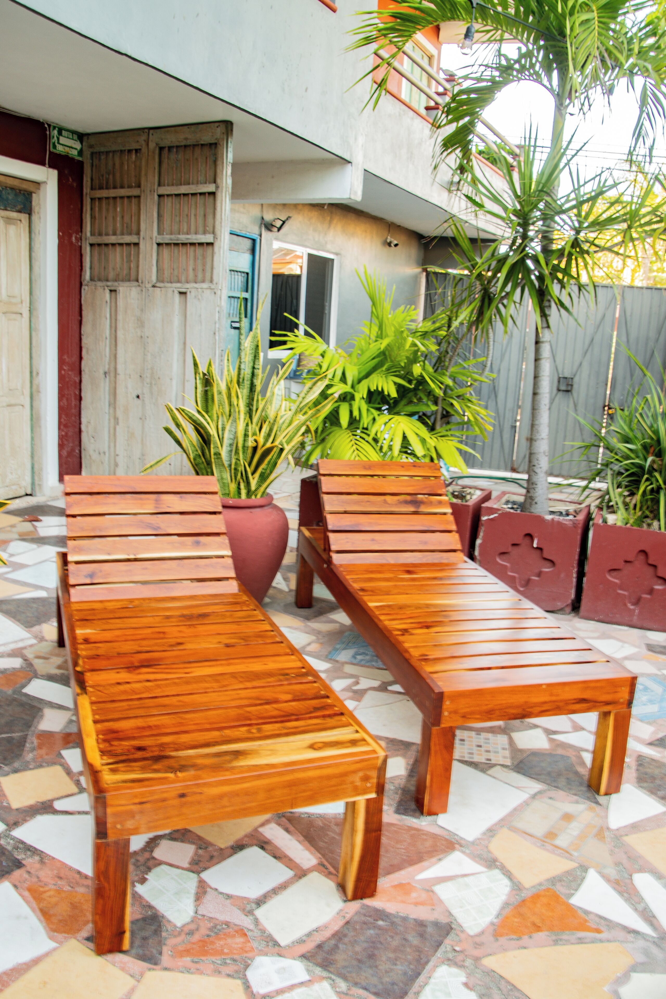 A wooden bench and table set on a tiled patio with potted plants.