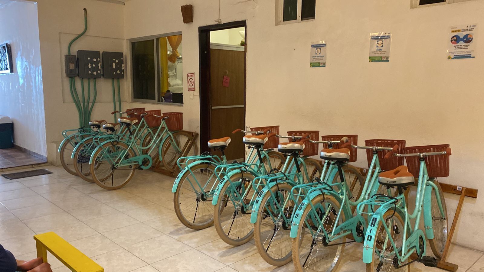 A row of turquoise bicycles with baskets, a door, and a wall with various signs.