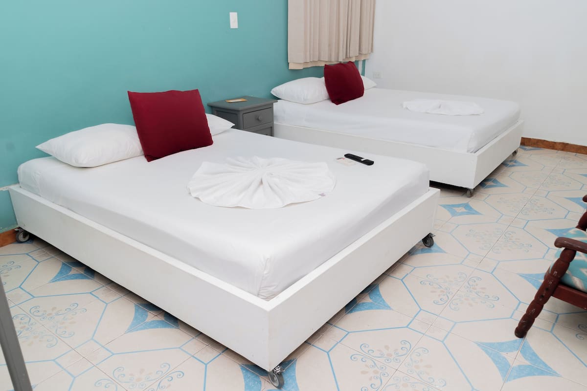 Two single beds with white bedding and red pillows, a small bedside table, and a chair.