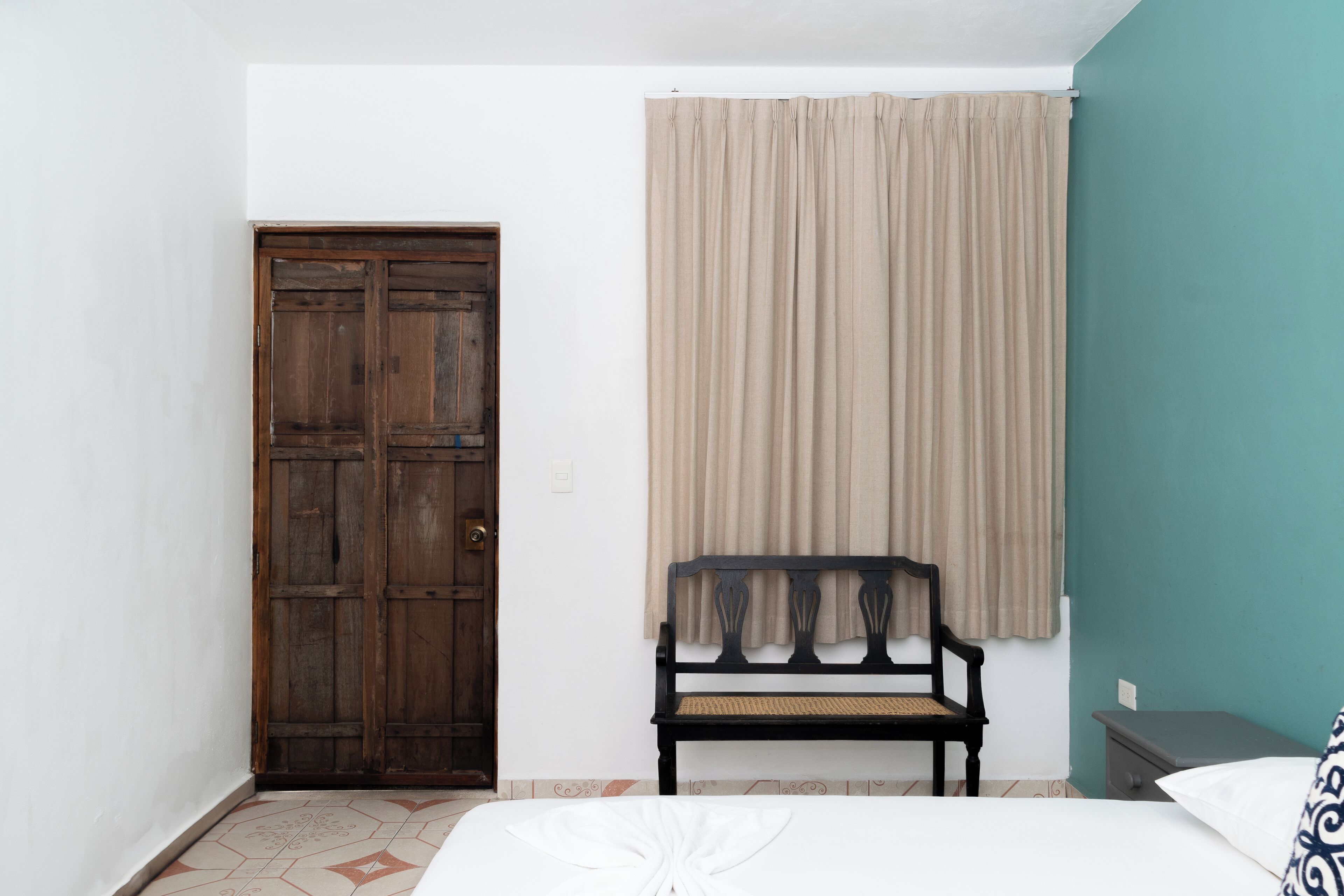 A room with a bed, a wooden wardrobe, a bench, and a window with curtains.