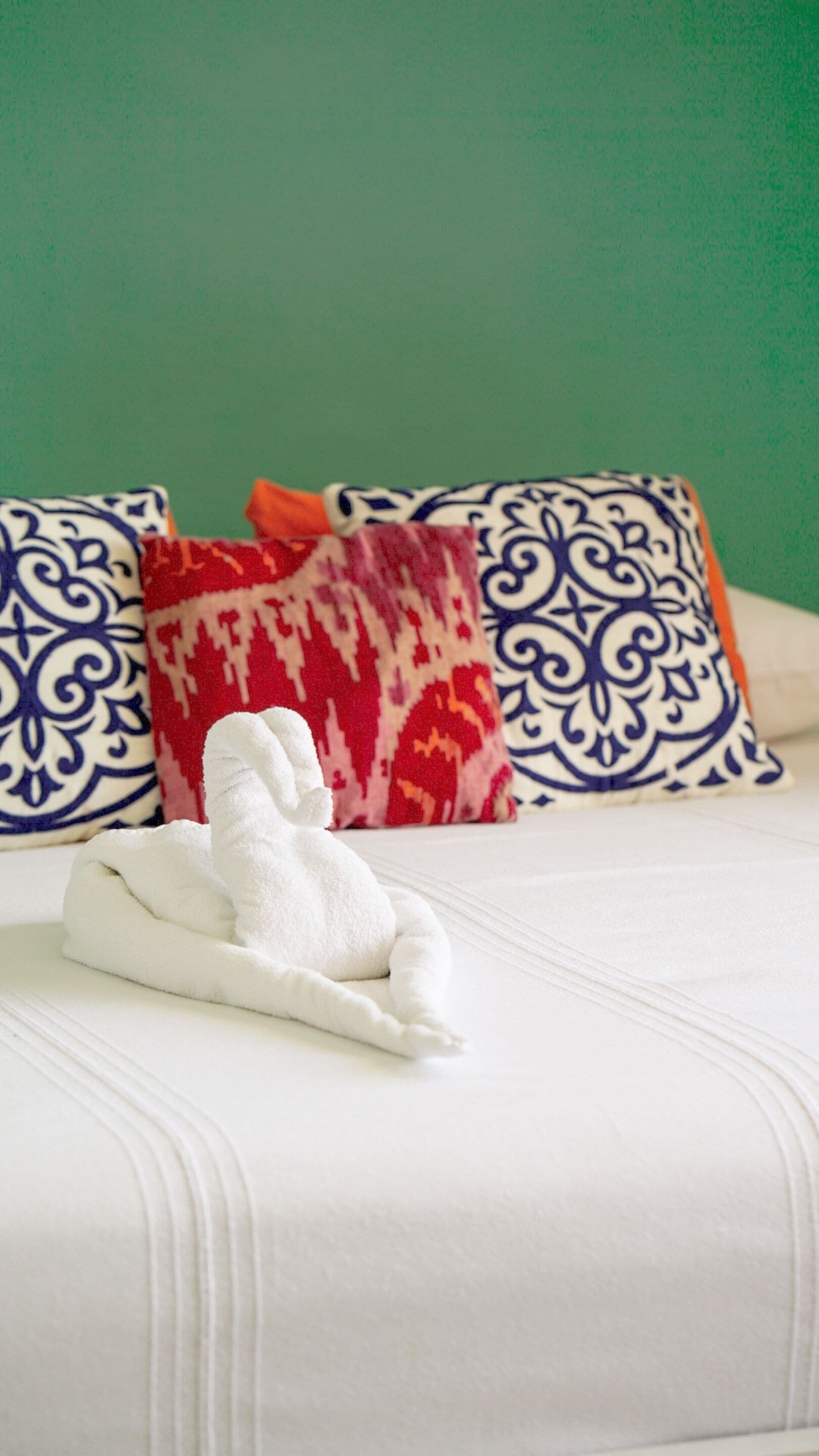 A neatly made bed with a white towel, two patterned pillows, and a red patterned pillow.