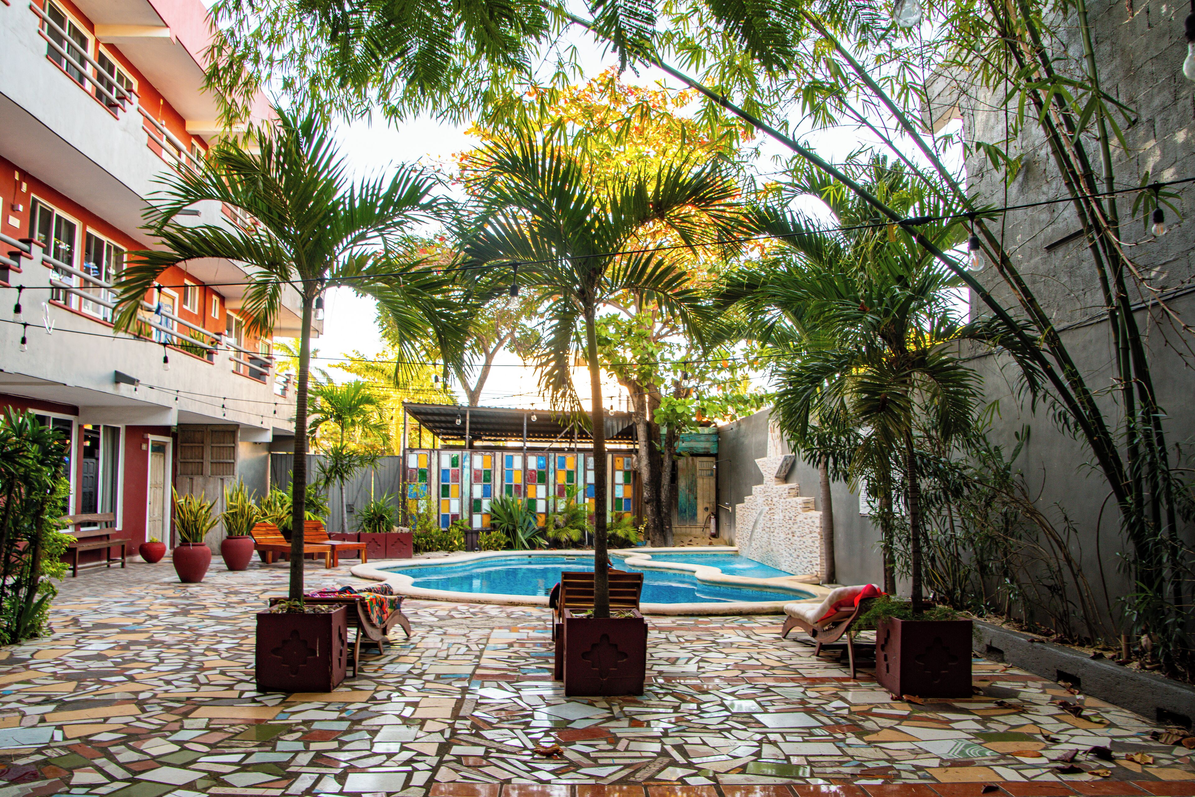 Un patio con piscina, suelo de baldosas y mobiliario exterior.