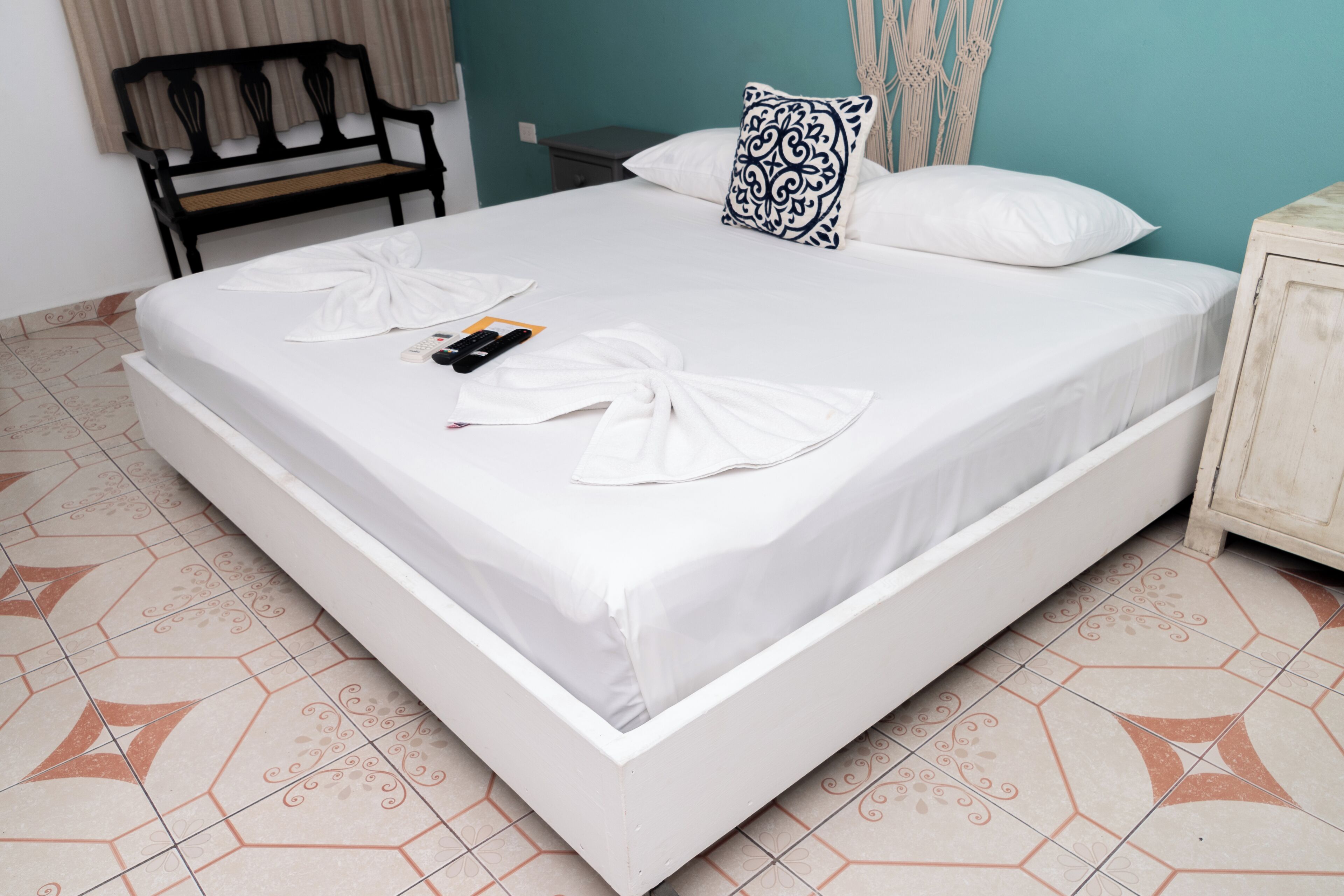 A neatly made bed with white linens, a remote control, and a towel on the bed.