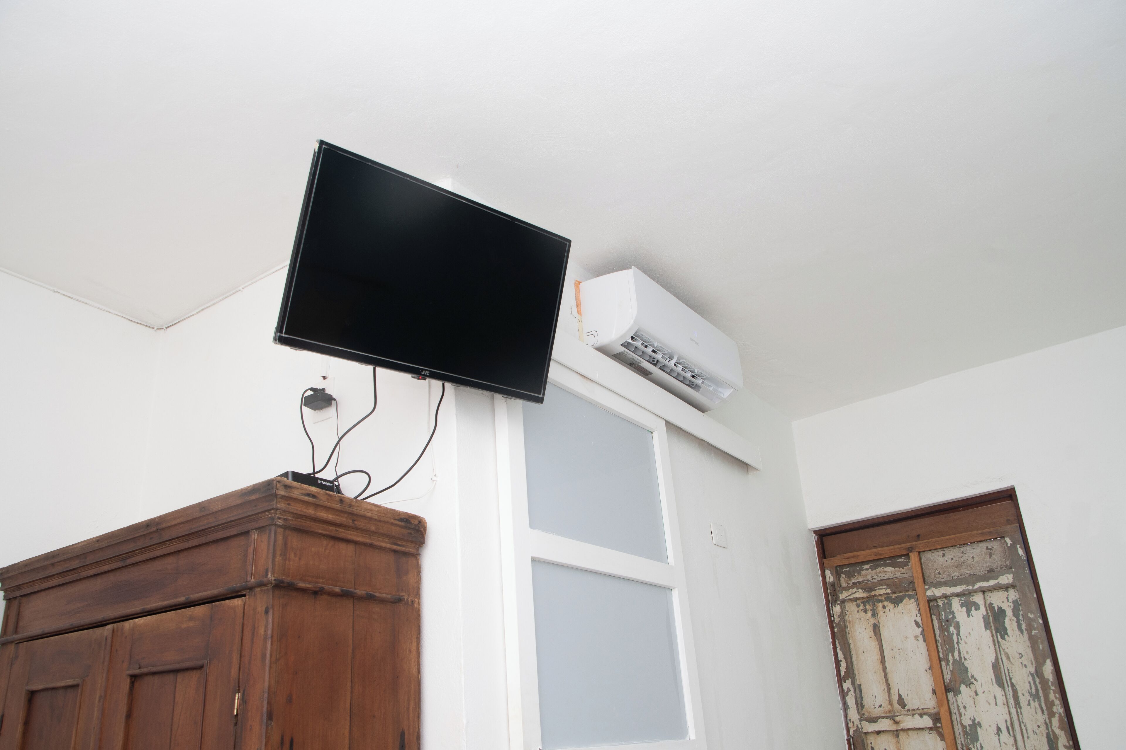 Habitación con televisor de pantalla plana en la pared, aire acondicionado blanco y un mueble de madera.