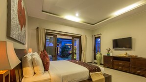 A well-lit bedroom with a large bed, a TV, and a view of the outdoors through a glass door. - Villa Katara (Seminyak)