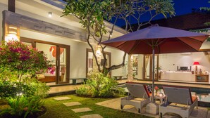 A well-lit outdoor area with a pool, lounge chairs, and a large umbrella providing shade. - Villa Katara (Seminyak)