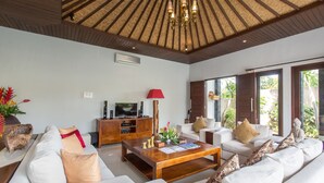 A modern living room with a wooden ceiling, a television, a coffee table, and white sofas. - Villa Katara (Seminyak)