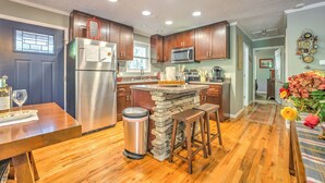 A kitchen with wooden cabinets, a stainless steel refrigerator, a stone island, and a wooden dining table.