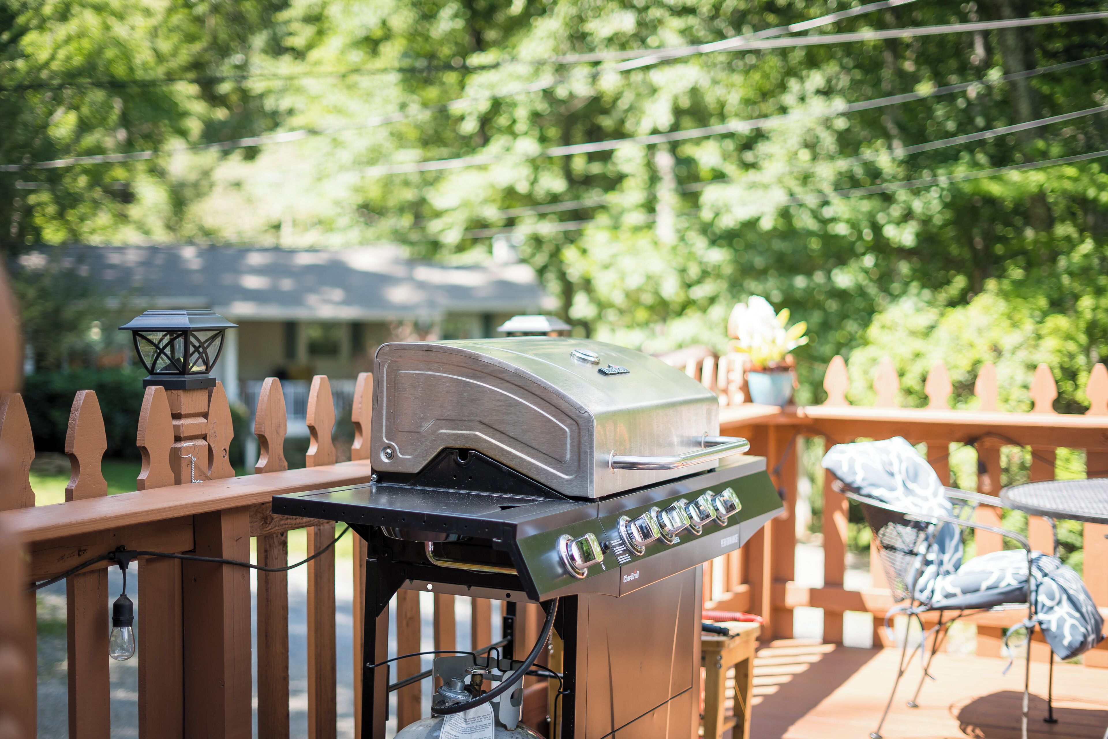 Una parrilla de barbacoa en una terraza exterior con un cerramiento de madera, una mesa y sillas.