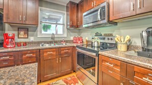 A kitchen with wooden cabinets, stainless steel appliances, granite countertops, and a window with blinds.