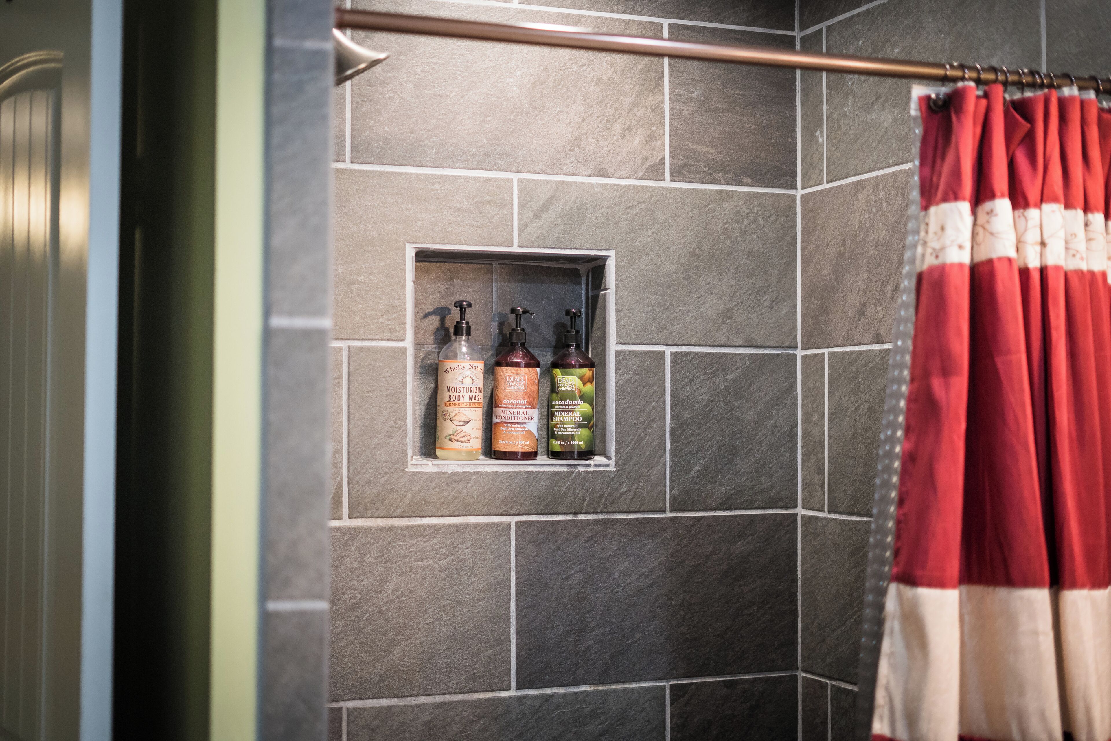 Ein Badezimmer mit Duschvorhang, Ablage für Toilettenartikel und gefliesten Wänden.