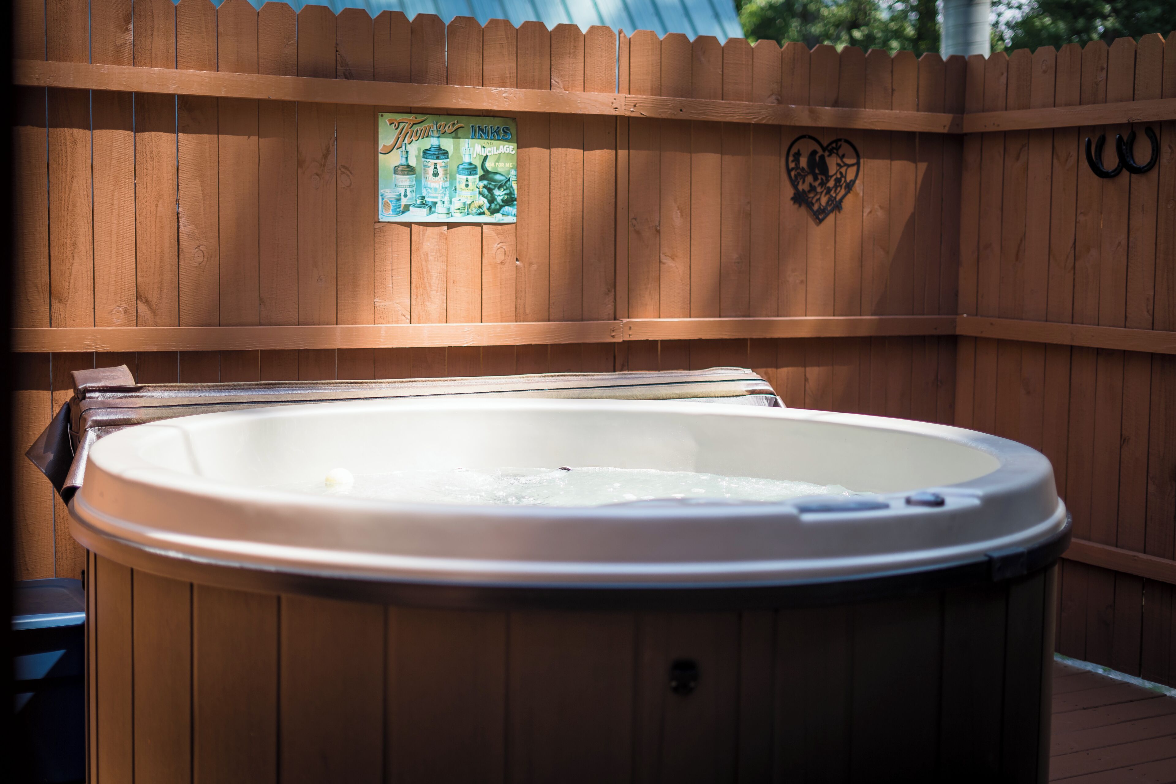 A hot tub in an outdoor wooden deck area with a wooden fence, a sign with a heart and horses, and a logo on the fence.