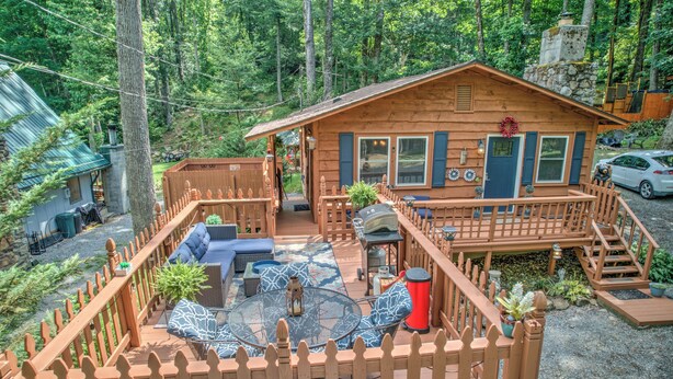 A cabin with a deck, outdoor seating, and a stone chimney.