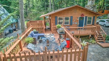 A cabin with a deck, outdoor seating, and a stone chimney.