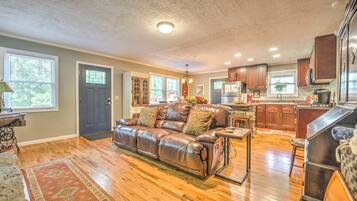 A spacious living room with a leather sofa, wooden flooring, and a kitchen area with wooden cabinets and a refrigerator.