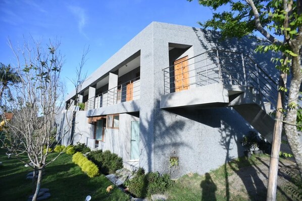 A modern building with a concrete facade, multiple balconies, and a well-maintained garden.