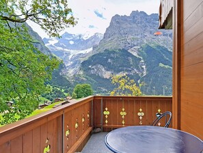 A balcony with a view of a mountainous landscape, a wooden railing with decorative cutouts, and a round table. - Firstsunne by Interhome (Grindelwald)