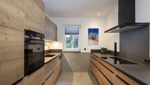 Une cuisine moderne avec des meubles en bois, un four encastré et une fenêtre donnant sur les arbres.