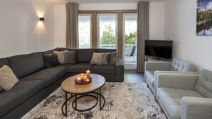 Un salon moderne avec un canapé d’angle, une table basse ronde ornée de bougies, un téléviseur à écran plat et un tableau accroché au mur.