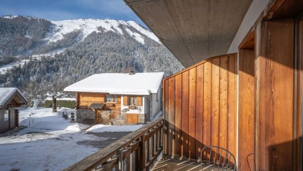 Ein Holzbalkon mit Blick auf einen schneebedeckten Berg und eine Hütte.