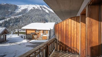 Un balcon en bois offrant une vue sur une montagne enneigée et un chalet.