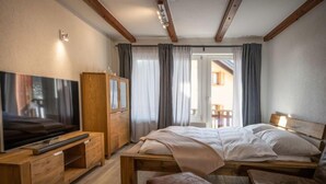 Ein modernes Schlafzimmer mit einem hölzernen Bett, einem Fernseher auf einem Holzschrank, einem Holzschrank und Blick auf einen Balkon.