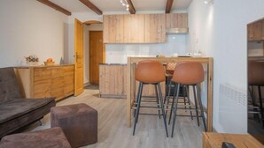 Eine moderne Küche mit Holzausstattung, eine Essecke mit zwei Hockern und ein Sofa in einem Wohnzimmer.