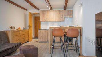 Une cuisine moderne avec des meubles en bois, un coin repas avec deux tabourets et un canapé dans le salon.