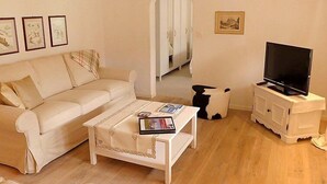 Un soggiorno con un divano beige, un tavolino da caffè con riviste, una televisione su un mobile bianco e un armadio sullo sfondo.