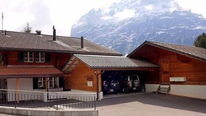 Un edificio in legno con garage, veicoli parcheggiati e montagne sullo sfondo.