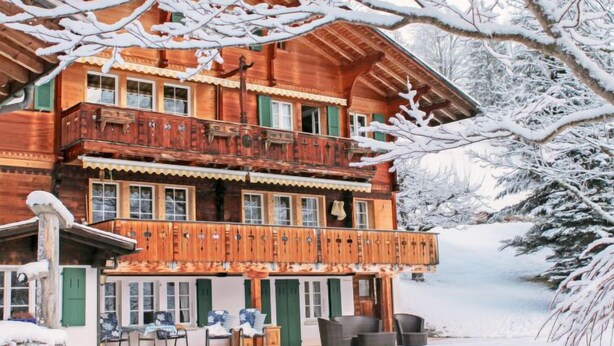 Una baita in legno con balcone, diverse finestre e un paesaggio innevato.