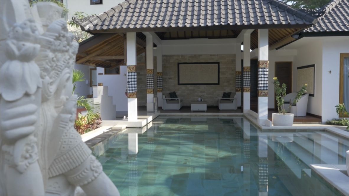 A swimming pool with a covered seating area, stone walls, and a statue.