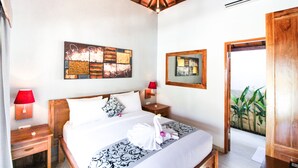 A hotel room with a bed, two bedside tables, a wall-mounted air conditioner, and a door leading to a balcony with plants. - Villa Casablanca Surf Keramas (Gianyar)