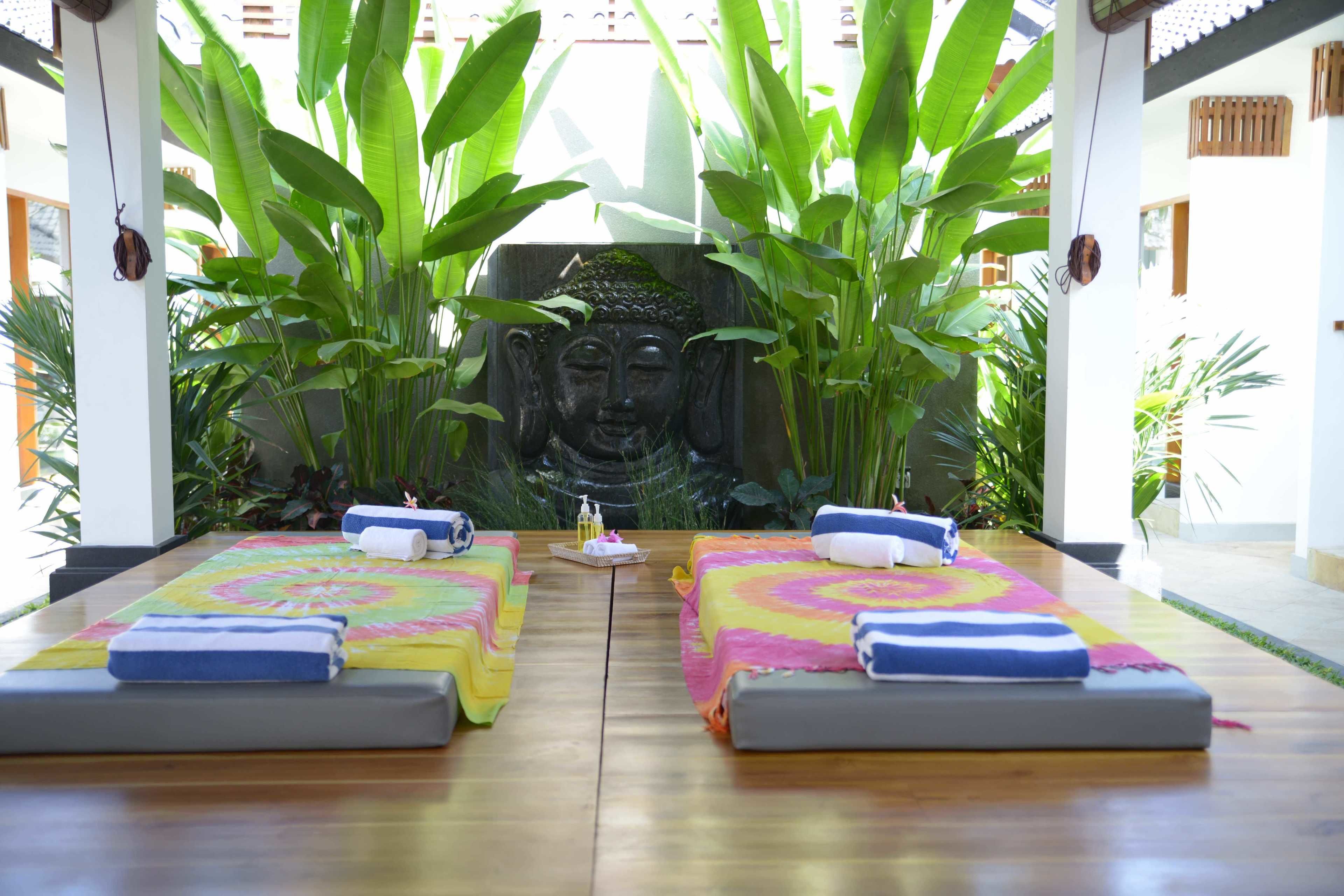 Una habitación con dos camillas de masaje, una estatua de Buda y abundante vegetación.