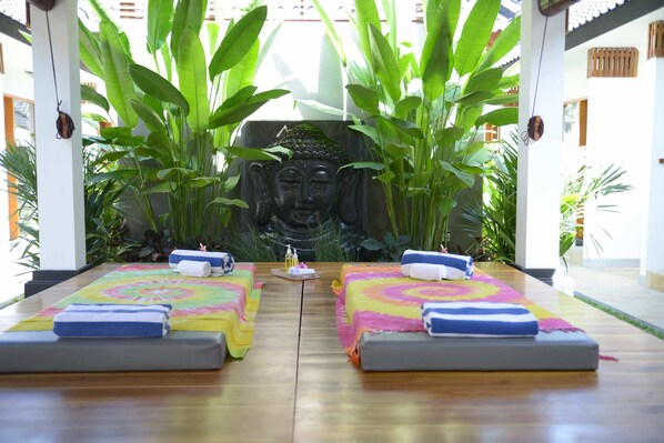 A room with two massage beds, a Buddha statue, and lush green plants.