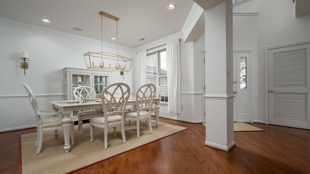A dining area with a white table and chairs, a chandelier, and a view of the outside. - 36 Old Mill Way, Bayside at Bethany Lakes - 4 Bedroom Luxury w/Community Pool (Ocean View)